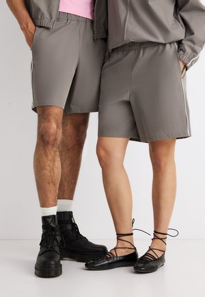 Dvije osobe nose iste sive kratke hlače; jedna nosi crne čizme s vezicama i bijele čarape, druga crne balerinke s vezicama.