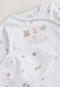 Vit babyoutfit och hatt med djuransikten och texten "born in 2026" broderad i mjuka beige och grå toner.