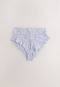 Sous-vêtement en dentelle blanche taille haute avec motif floral et bords festonnés, posé à plat sur un fond beige clair.