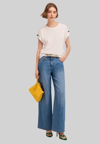 Vit kortärmad skjorta, högmidjade vida blåjeans, gul handväska, gröna klacksandaler. Avslappnad outfit med kontrasterande färger.