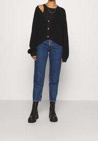 Cardigan negro de punto con escote en V y tres botones, combinado con jeans azules de talle alto. Botas negras con cordones completan el look.