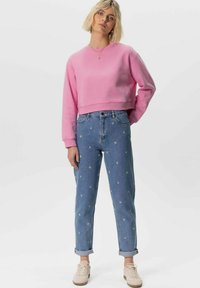 Sweatshirt rose court avec ourlet côtelé, associé à un jean en denim bleu clair avec des motifs d'étoiles et des poignets retournés. Des baskets beiges complètent le look.