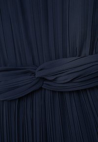 Marineblaue Faltenkleid aus strukturiertem Stoff mit einem geknoteten Bindedetail an der Taille, das eine strukturierte Silhouette schafft.