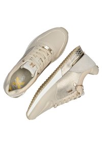 Beige tenisky s koženými a texturovanými kovovými akcenty. Mají šněrovací design, tvarovanou podrážku a dekorativní řetěz blízko paty.