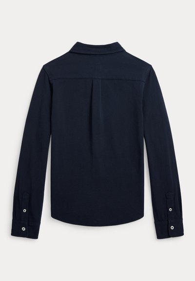 Navy mėlynos spalvos ilgomis rankovėmis marškiniai su sagomis rankogaliuose, siūle nugaroje ir centrinė apversta klostė, rodoma iš nugaros.