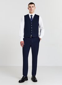 Marinblauer Dreiteiler mit Weste, vorne geknöpft, kombiniert mit einem weißen Dressshirt und einer gestreiften Krawatte. Schwarze Schuhe runden den Look ab.
