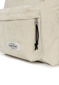 Kordurový batoh v krémové barvě s černým zipem. Disponuje horizontálně ribbovanou texturou a štítkem s logem Eastpak.