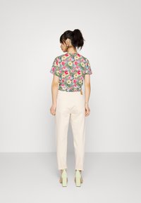 Top cropped floral com flores rosa-brilhante e amarelas num fundo verde, combinado com calças rosa-pálido e sapatos de salto verde-mint.