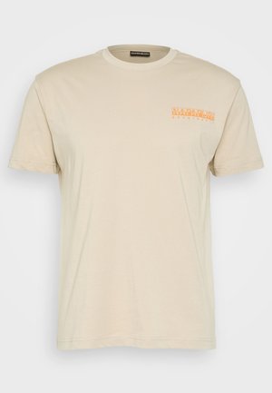 Personne portant un gilet utilitaire vert olive, un t-shirt beige, un short de cyclisme noir avec des logos blancs, des baskets blanches, des chaussettes rayées et une pochette en bandoulière.