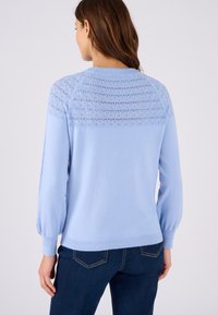 Maglione a girocollo azzurro chiaro con un motivo a maglia texturizzato sulla spalliera. Presenta maniche lunghe e un orlo a costine. Abbinato a jeans blu scuro.