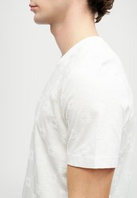 Tricou alb din bumbac, cu un model floral texturat, decolteu rotund, mâneci scurte, tăiere slim și finisaj neted.