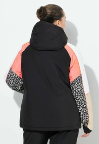 Černá a korálově červená bunda s kapucí a vzorovanými rukávy. Má barevné blokování, elastické manžety a měkkou texturu.