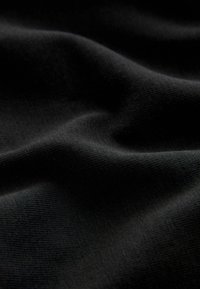 Tela negra con una superficie suave y texturizada, que presenta suaves olas y un patrón de tejido consistente. Apariencia suave y ligera.