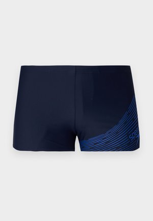 Bañador color azul marino oscuro con una textura suave, que presenta un diseño gráfico lineal azul en el lado derecho. Corte estándar sin elementos metálicos.