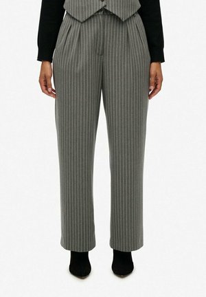Pantalons à rayures grises avec une coupe ajustée, des plis à l'avant et des jambes larges et plates. Portés avec un haut noir et des bottines noires.