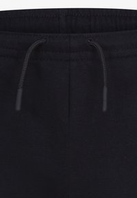 Pantalones de chándal negros con una textura suave, que cuentan con una cinturilla elástica, cordón y detalles de costura sutiles. Adecuados para uso casual.