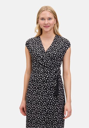 Zwarte jurk met een wikkelontwerp, korte cap sleeves en een wit gespikkeld patroon. Heeft een strik in de taille voor een figuurvormend silhouet.