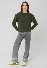 Un pull en tricot vert avec un col rond et des épaules tombantes, associé à un jean large gris clair et des baskets crème.