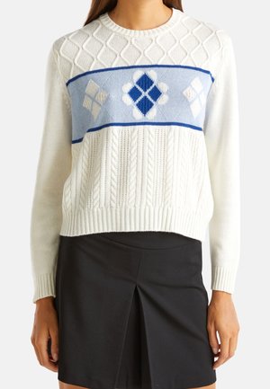 Hvid strikket sweater med et tekstureret kabeldesign, en blå bæltedragt med diamanter og en ribbet kant. Sammen med en sort nederdel.
