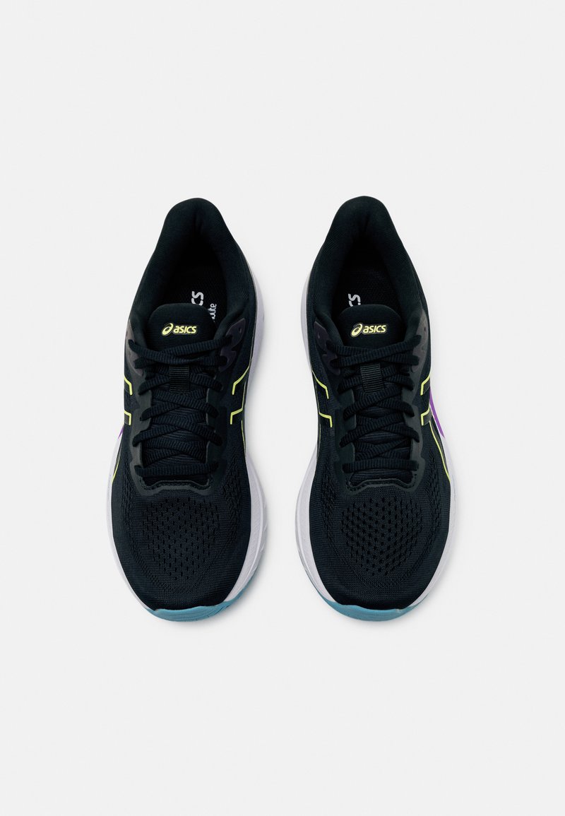 Zapatillas deportivas negras con parte superior de malla, acentos en amarillo y púrpura, diseño con cordones y suela blanca con una suela exterior azul clara.