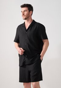 Svart T-skjorte med kort arm laget av teksturert stoff, med lomme og knappestolpe, kombinert med matchende svarte shorts.