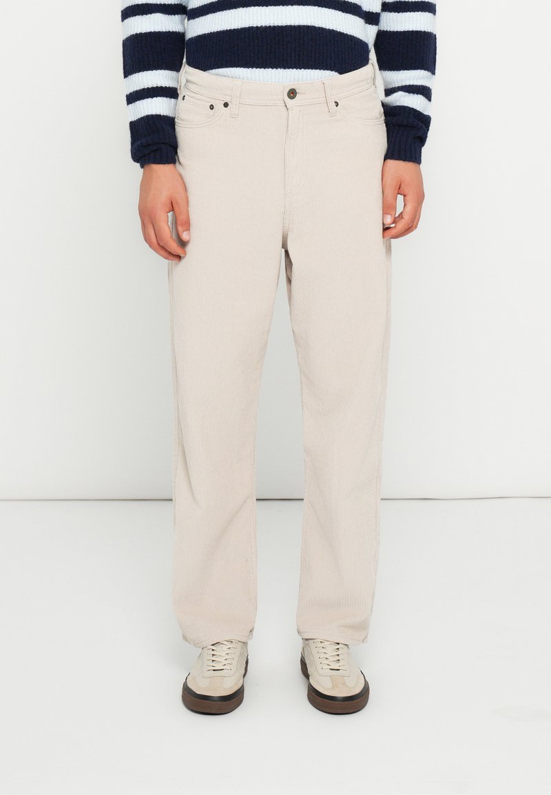 Beige corduroy pants with a straight-leg fit, featuring visible stitching and two front pockets. Worn with a navy and white striped sweater.