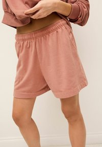 Pantalones cortos de mezcla de algodón en color rosa claro, con cintura elástica y bolsillos laterales. Textura suave, largo hasta la mitad del muslo, dobladillos acabados.