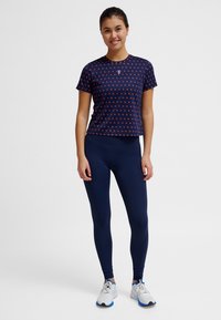 Marinblå sport-T-shirt med rött mönster, kombinerad med marinblå leggings och vita sneakers. Tyget verkar slätt, figurnära design, korta ärmar.