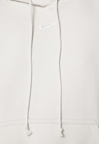 Balta Nike džemperis su kapuce, reguliuojama virvele, raukšlėmis rankovėmis ir apykakle, mažas siuvinėtas logotipas ant krūtinės. Minkšta medžiaga, standartinio kirpimo.