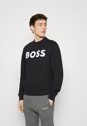 Felpa nera con logo "BOSS" bianco, scollatura rotonda, maniche lunghe e polsini a costine. Abbinata a pantaloni sportivi grigi con tasca con zip.