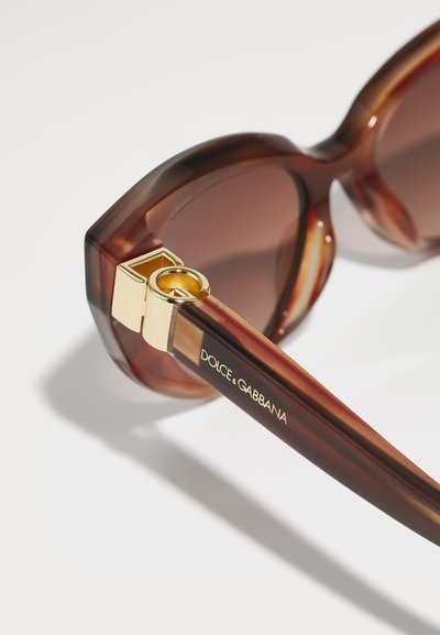 Kareivinės saulės akiniai su tamsiais objektyvais. Stori kampuoti rėmeliai, auksiniai akcentai ant vyriuko ir "Dolce & Gabbana" įgraviruotas ant šakės.