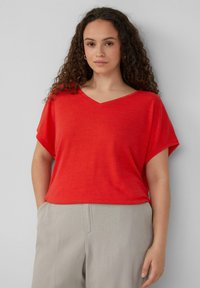Rode V-hals t-shirt van een zachte, ademende stof met brede korte mouwen. Draag het met lichtgrijze, losse broek.