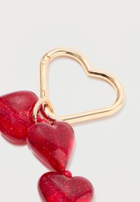 Red acrylic hearts connected by a shiny gold heart-shaped metal clasp. The hearts feature a sparkly texture and smooth finish.