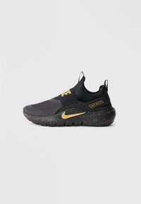 Fekete és arany slip-on Nike sportcipő, pöttyös talppal, rugalmas pánttal a "Nike" felirattal és "Just Do It" címkével az oldalsó paneleken.