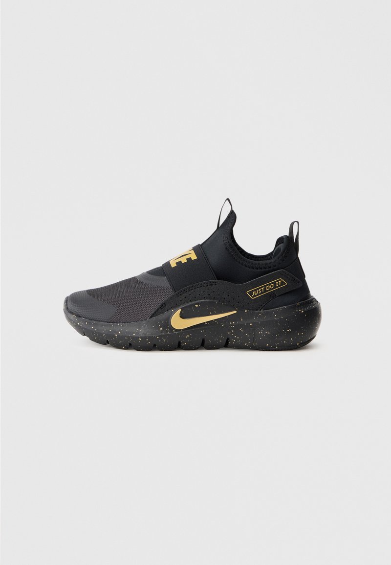 Fekete és arany slip-on Nike sportcipő, pöttyös talppal, rugalmas pánttal a "Nike" felirattal és "Just Do It" címkével az oldalsó paneleken.
