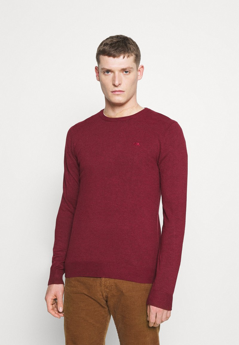 Weinroter Langarm-Pullover aus Strickstoff. Mit rundem Ausschnitt und einem kleinen Logoakzent auf der Brust. Glatte Textur.