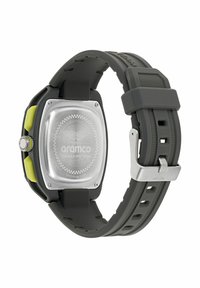 Pelēks gumijas siksniņas pulkstenis ar kvadrātu formas sudraba korpusu, dzelteniem akcentiem un rakstainu aizmuguri, kurā ir zīmola logo un Formula One komandas detaļas.