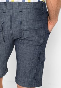 Pantaloni cargo in denim blu scuro, con molteplici tasche laterali, cuciture in vista e una vestibilità dritta con orlo al ginocchio.