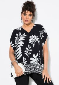 Schwarzes Oberteil mit weißem Blumenmuster, V-Ausschnitt, kurzen Ärmeln und einem akzentuierten Saum. Kombiniert mit einer weißen Clutch.