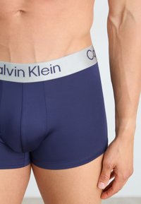 Marineblauwe boxershorts met een zachte, elastische zilveren tailleband met het label "Calvin Klein." Kenmerkt zich door een gladde stof en een aansluitend ontwerp.