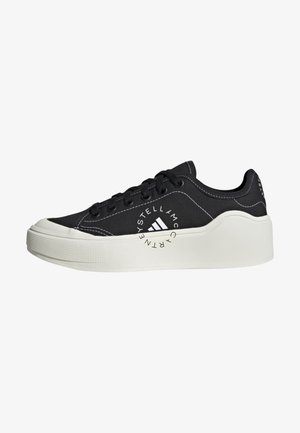 Zapatilla negra de corte bajo con suela plataforma blanca gruesa, cordones negros, costuras blancas y logo circular en el lateral con la inscripción "Stella McCartney."