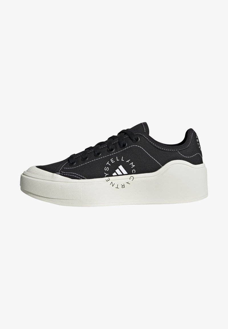 Baskets basses noires avec semelle plateforme blanche épaisse, lacets noirs, coutures blanches et logo circulaire sur le côté indiquant « Stella McCartney ».