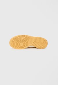 Nike sneakersåle med et teksturert gummidesign i lys tan. Har sirkel- og rutenettmønstre for grep. Flat overflate og slitesterkt materiale.