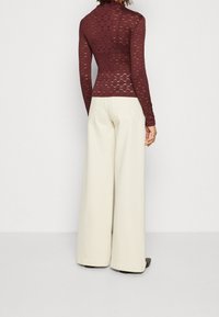 Burgundy texturerad långärmad topp kombinerad med vida beiga byxor. Toppens design har ett mönster och en hög halsringning.