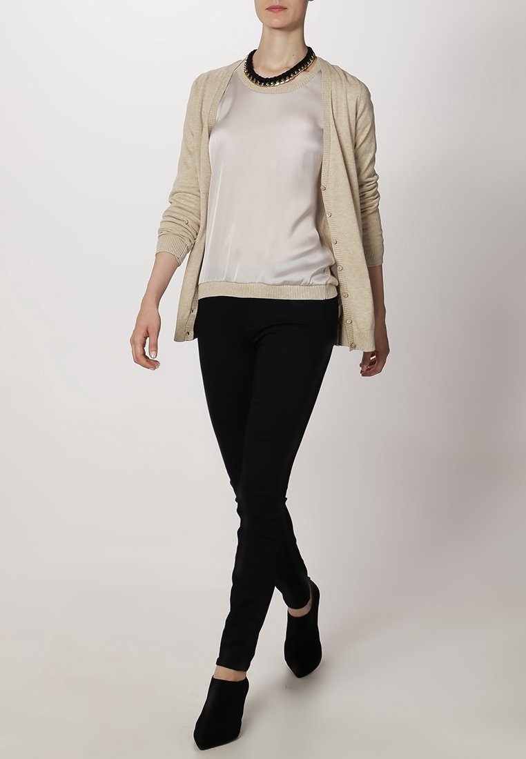 Beige cardigan over a light silk blouse, paired with black slim-fit pants and ankle booties, featuring a bold statement necklace.