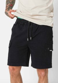Pantaloni cargo neri in cotone con vita elastica, cordino regolabile e tasche laterali con chiusure a bottone.