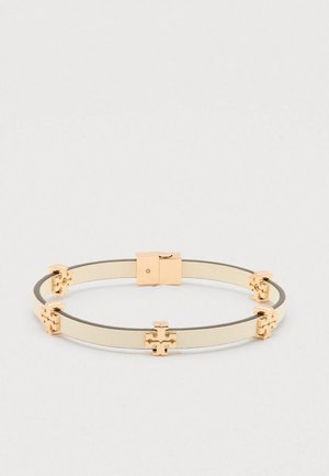 Béžový kožený náramok s pozlátenými krížovými akcentmi rovnomerne rozmiestnenými a s obdĺžnikovou zlatou sponou na jednoduchom pozadí.