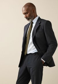 Marineblauer Anzug mit maßgeschneiderter Passform, hellblauem Hemd und strukturiertem olivgrünem Krawatte. Glatter Stoff, Zweiknopfjacke und elegante Silhouette.