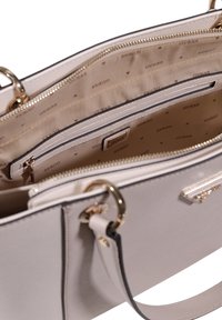 Beige käsilaukku, jossa on teksturoitu materiaali, kullattu varustelu ja useita lokeroita, vuorattu brändin kuviollisella kankaalla.