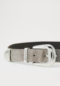 Ceinture en métal argenté texturé avec une boucle brillante en argent ; présente un motif en losanges et un intérieur noir lisse.